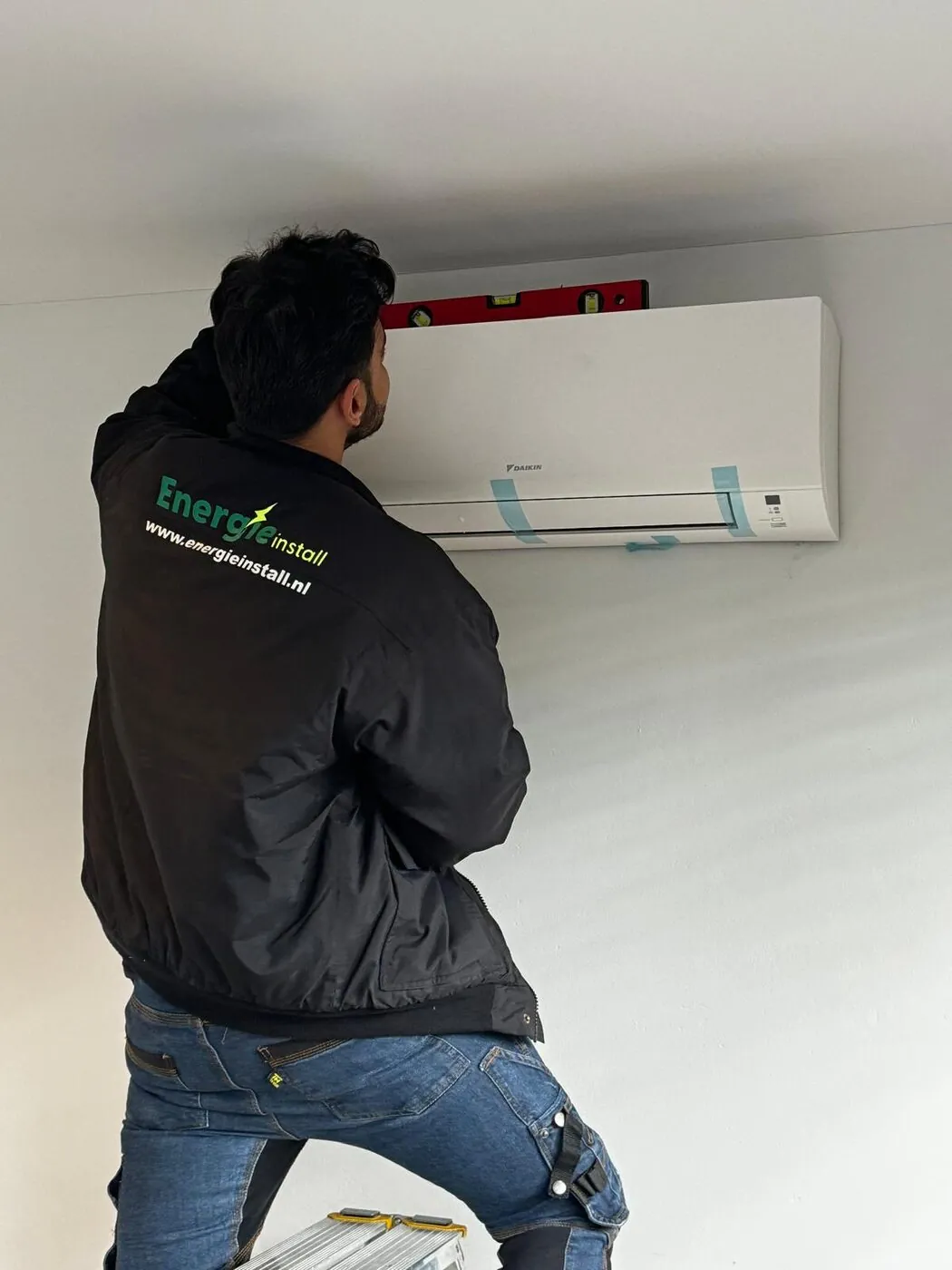 Monteur stelt een airco binnenunit waterpas af tijdens montage aan de muur