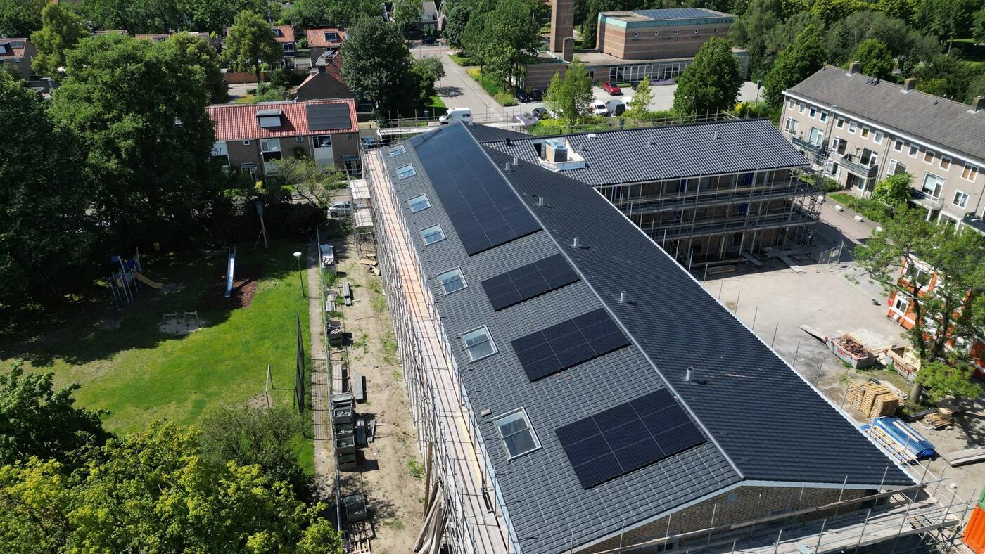 Luchtfoto van zonnepanelen op een schuin pannendak van een gebouw in een groene woonwijk