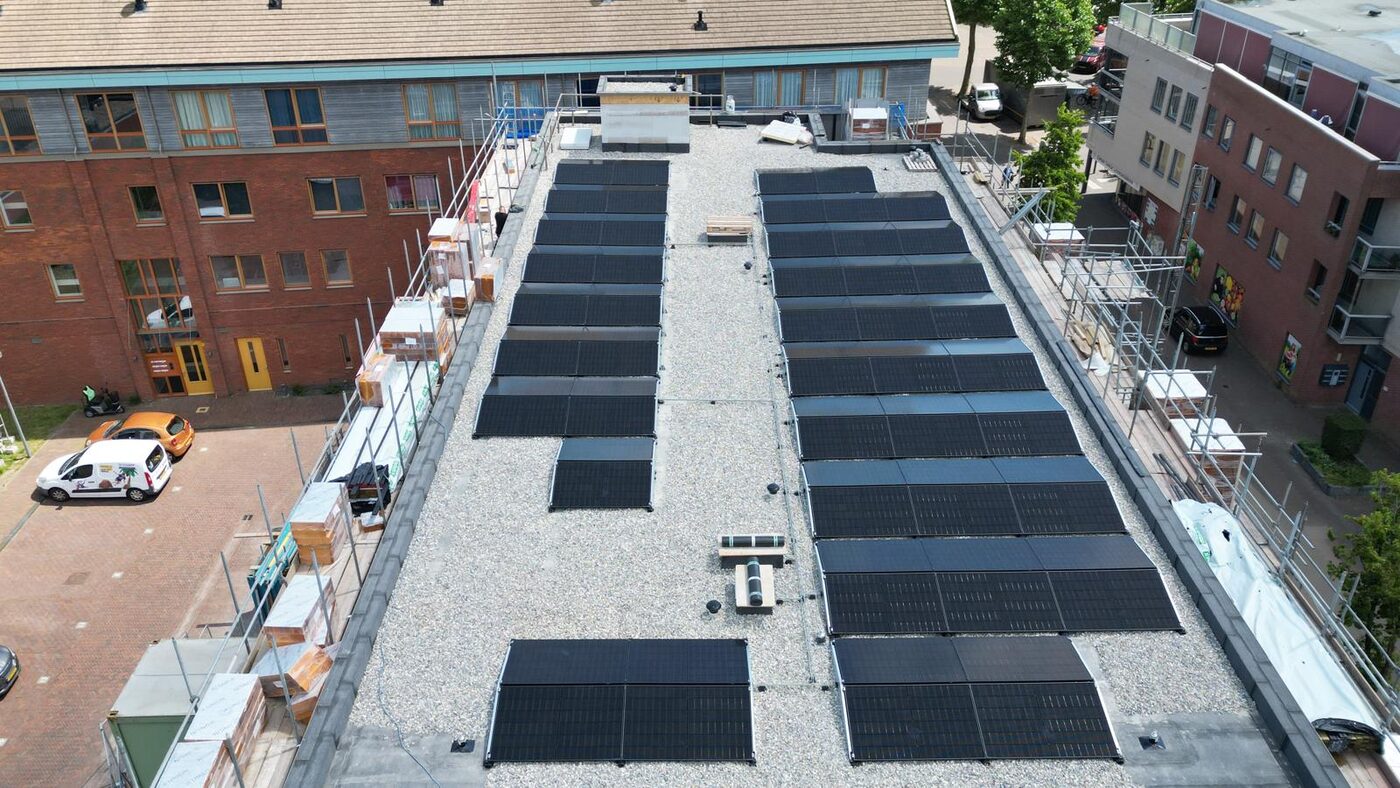 Drone-luchtfoto van zwarte zonnepanelen geinstalleerd op het platte dak van een appartementencomplex tijdens een installatieproject