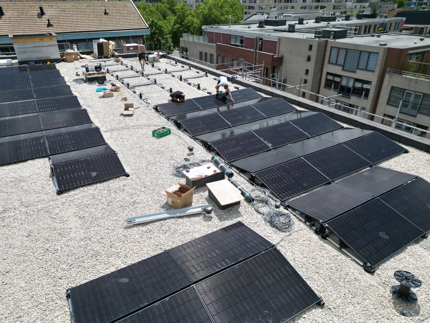 Luchtfoto van zonnepanelen installatie in aanleg op het platte dak van een groot gebouw met monteurs aan het werk