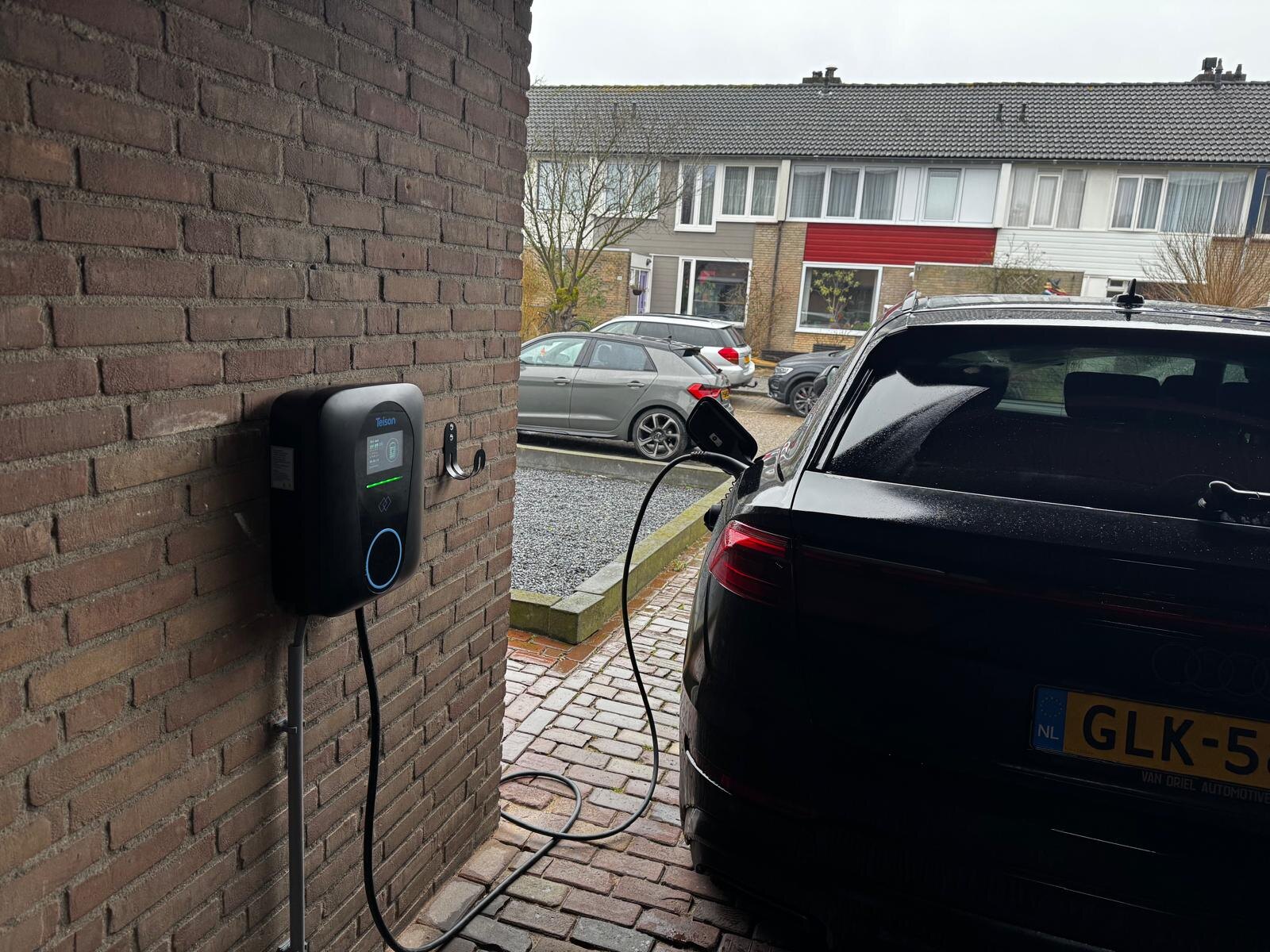 Elektrische auto wordt opgeladen aan een wandlaadpaal bij een woning in een woonstraat