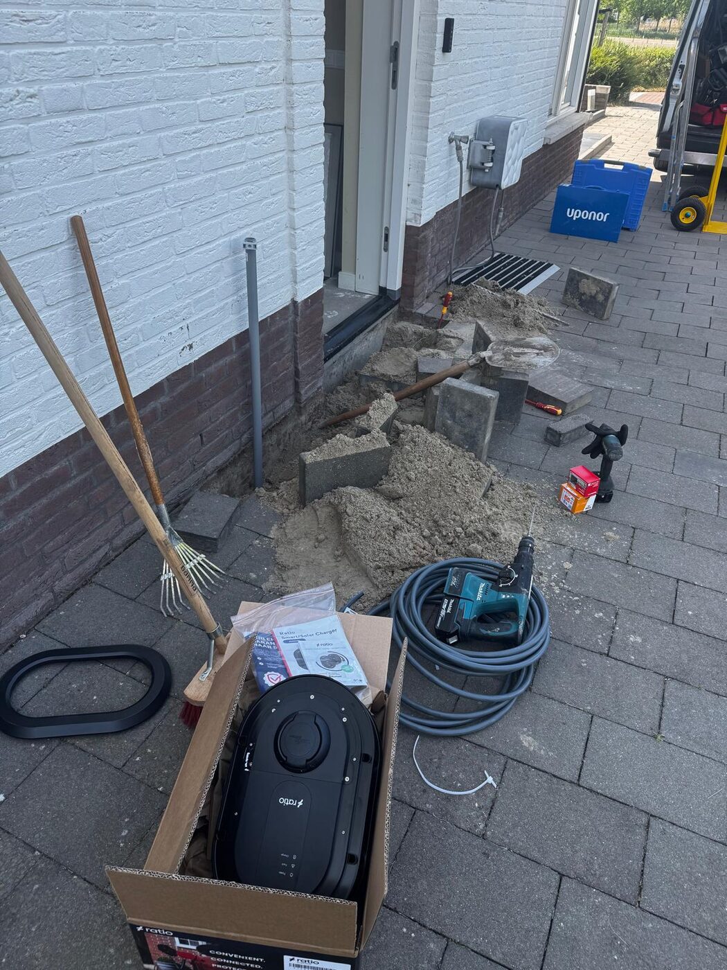 Installatie van een laadpaal aan de gevel met graafwerk voor de stroomkabel boormachine en nieuwe laadpaal in de doos