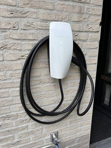 Wandlaadpaal met opgerolde laadkabel gemonteerd aan een bakstenen gevel naast de voordeur
