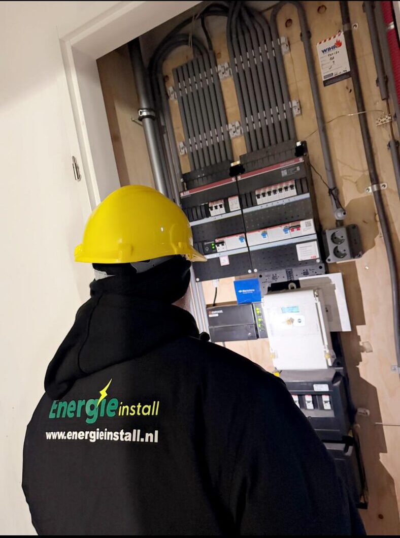 Monteur van Energie Install in bedrijfskleding werkt met gele veiligheidshelm aan een grote elektrische groepenkast