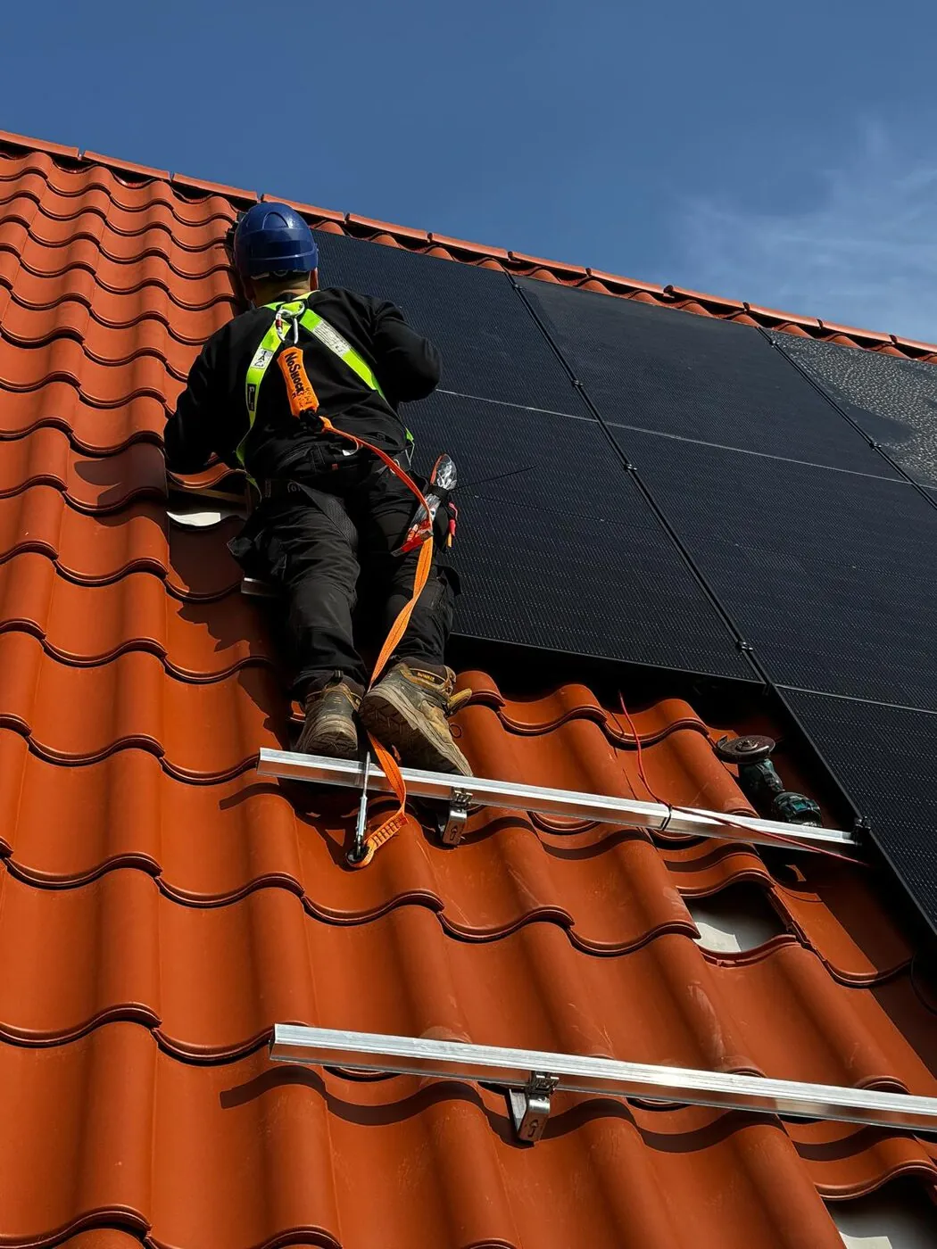 Monteur met veiligheidsharnas werkt aan zonnepanelen op een pannendak