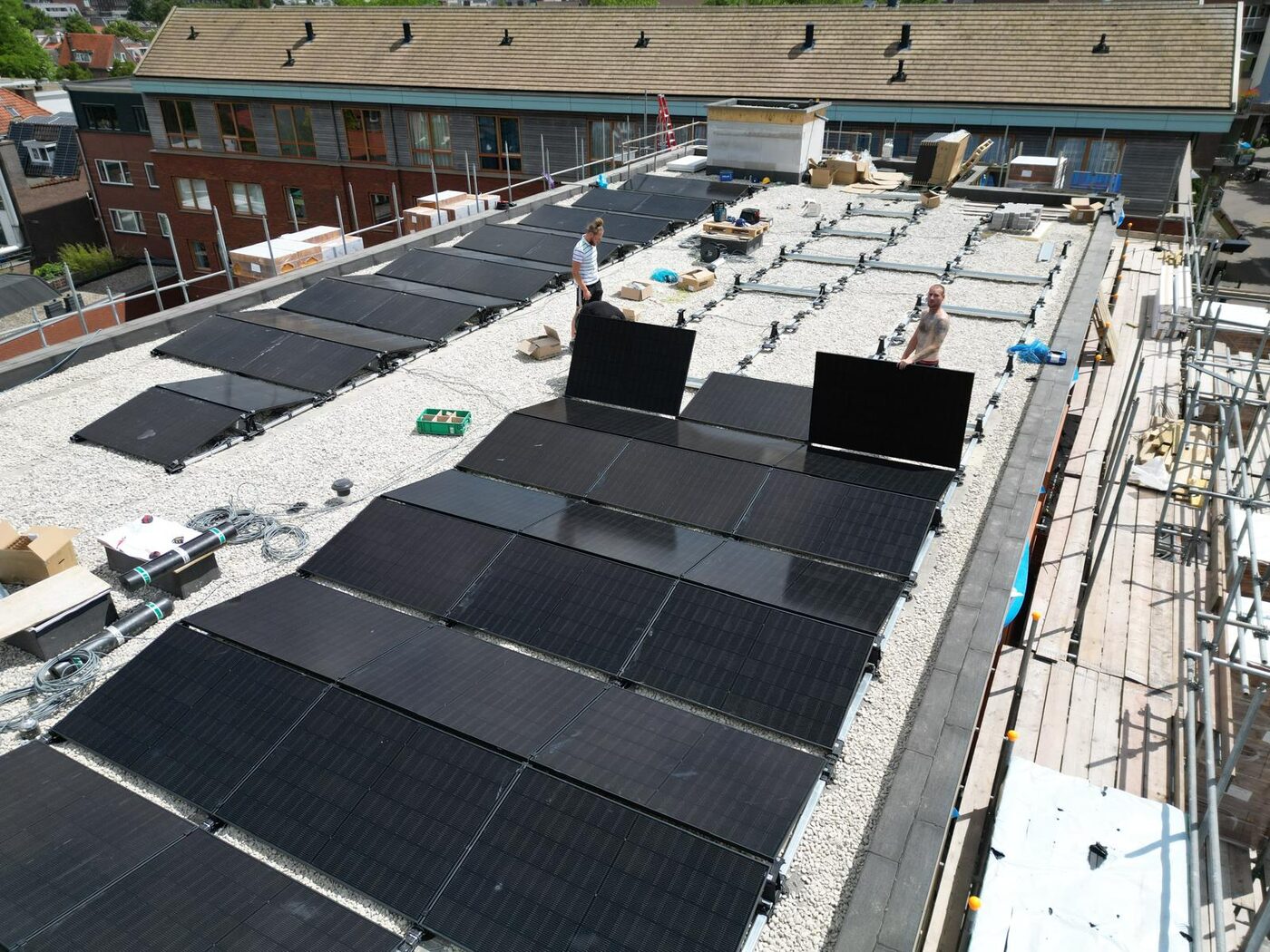 Monteurs plaatsen zwarte zonnepanelen op een grinddak van een groot pand tijdens de installatie