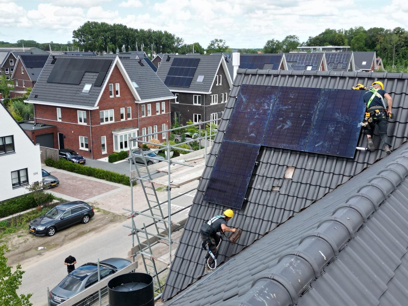 Monteurs met valbeveiliging installeren zonnepanelen op een schuin pannendak van een woning in een nieuwbouwwijk