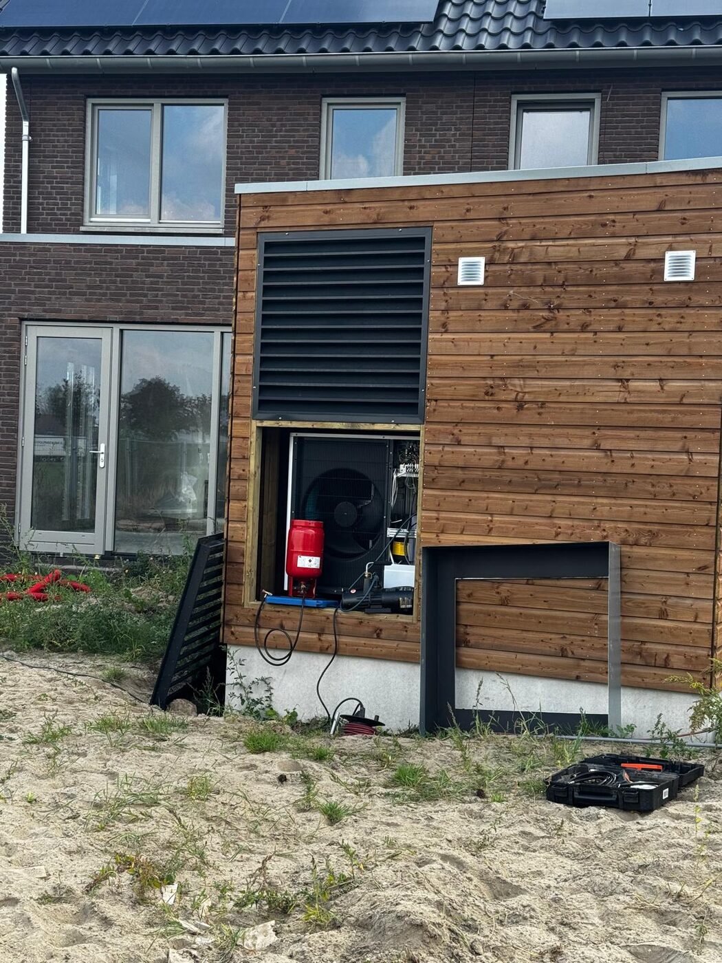 Warmtepomp-buitenunit weggewerkt in houten omkasting aan de gevel van een nieuwbouwwoning tijdens installatie