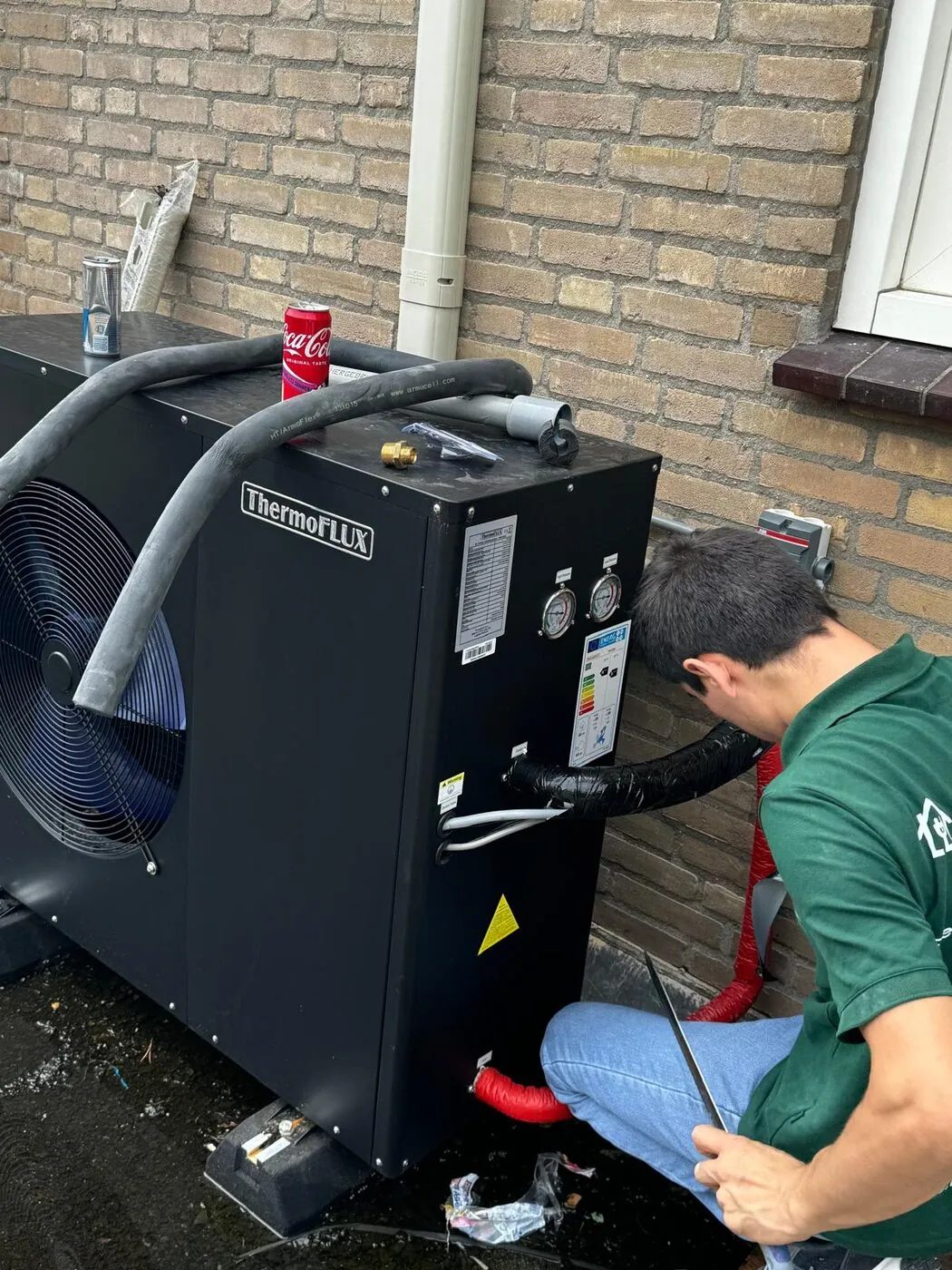 Monteur sluit een lucht-water warmtepomp buitenunit aan tegen de gevel