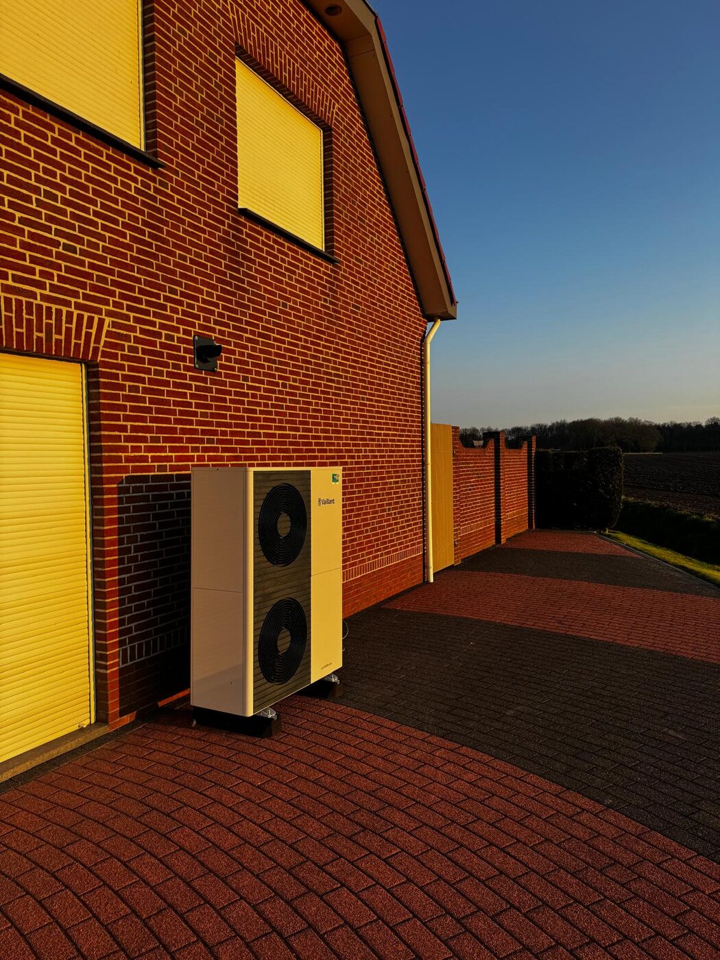 Lucht-water warmtepomp buitenunit geplaatst tegen rode bakstenen gevel van een vrijstaande woning