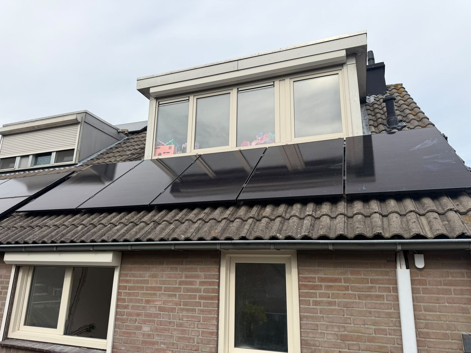Zonnepanelen op het dak naast een dakkapel van een woning