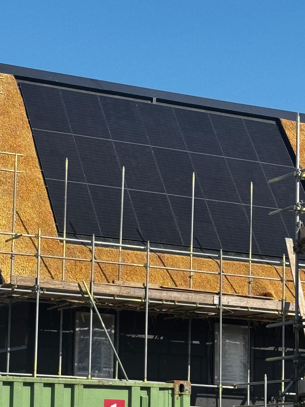 Full-black zonnepanelen op rietgedekt nieuwbouwdak in aanbouw met steiger tegen blauwe lucht