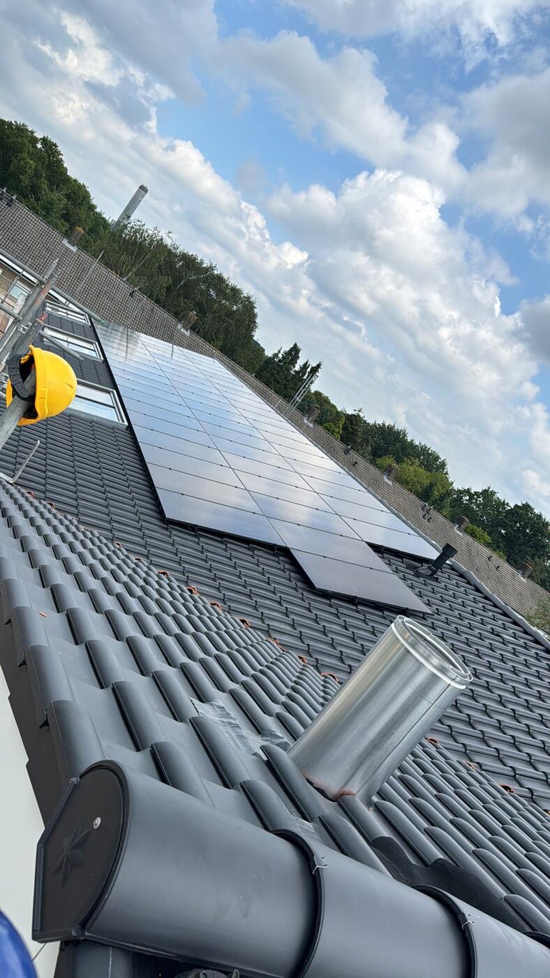 Zonnepanelen op grijs keramisch pannendak met monteur op steiger en RVS schoorsteenpijp tijdens installatie