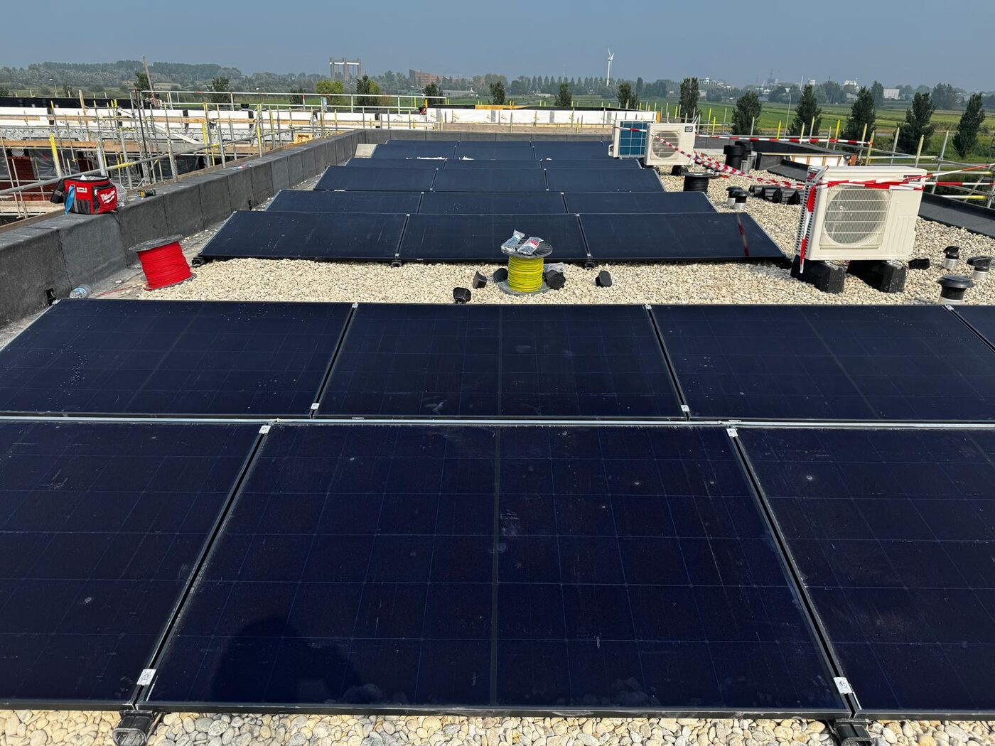 Rijen zonnepanelen in oost-west opstelling op een plat grinddak met uitzicht over polderlandschap