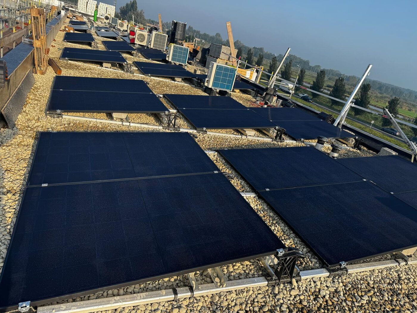 Zwarte zonnepanelen in oost-westopstelling op plat dak met grindballast bij utiliteitspand