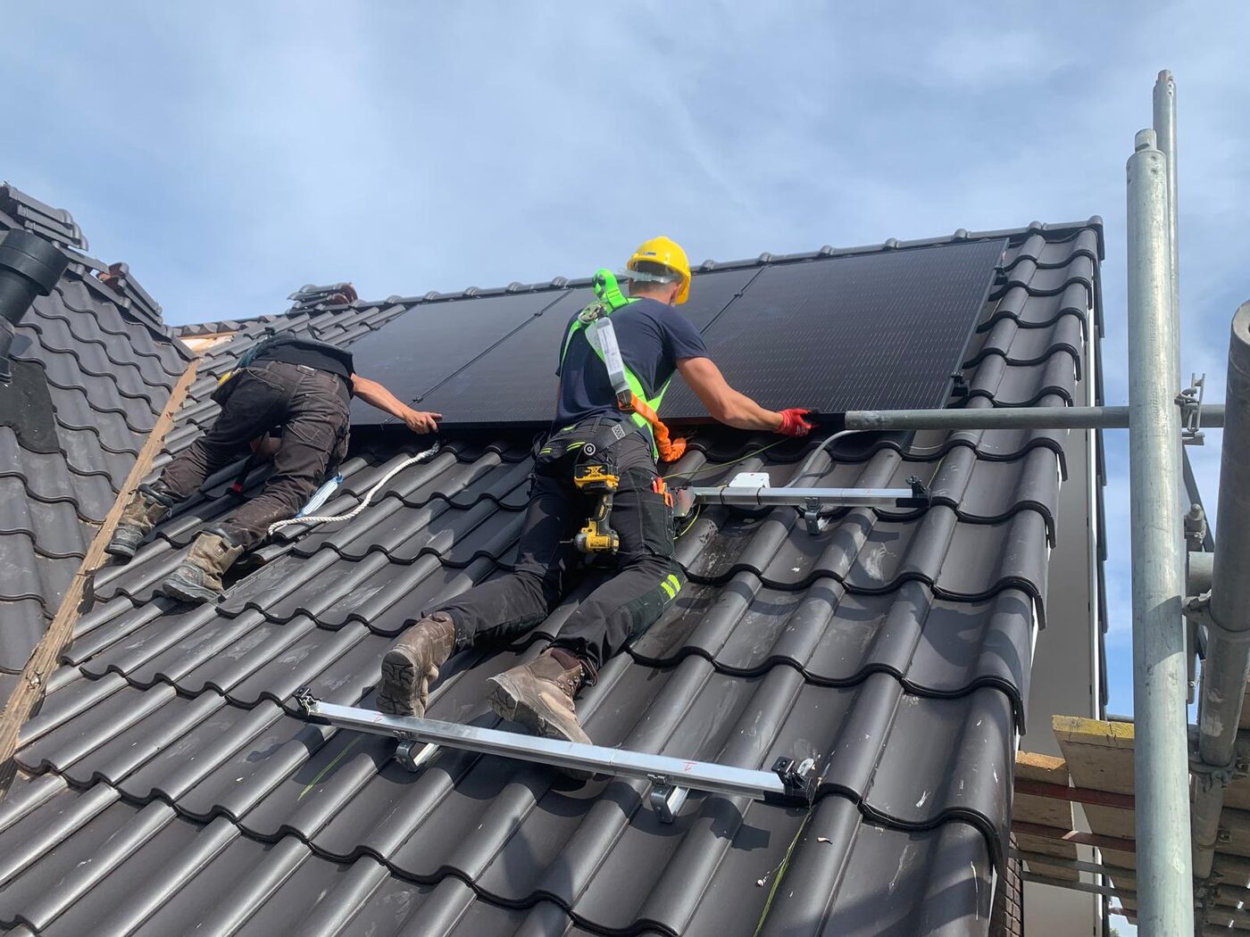 Monteurs met veiligheidsharnas installeren zwarte zonnepanelen op schuin dak met dakpannen