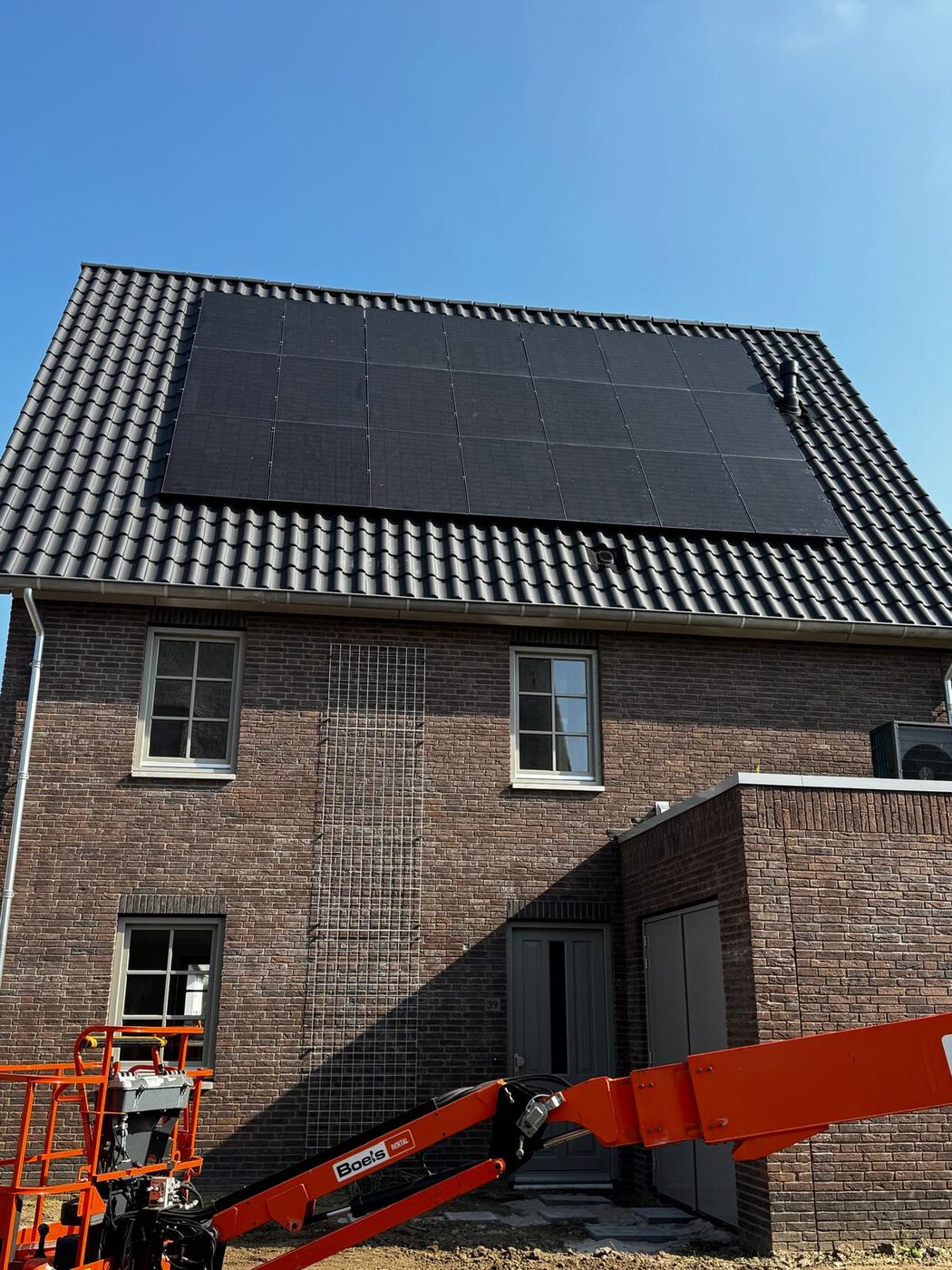 Zwarte zonnepanelen op het schuine pannendak van een nieuwbouwwoning onder een strakblauwe lucht
