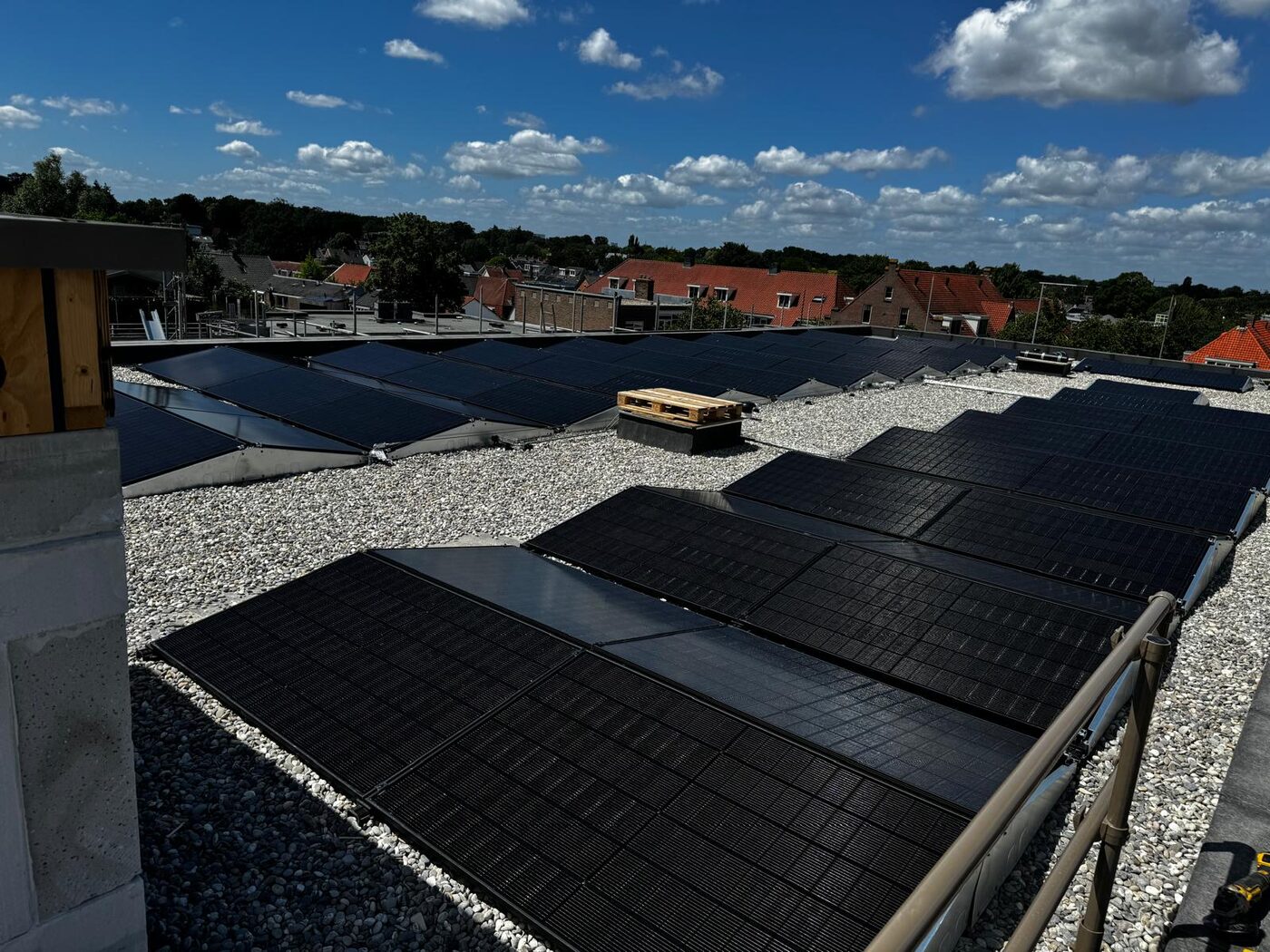 Groot zonnepanelenveld op een plat dak onder blauwe lucht met uitzicht over een dorp