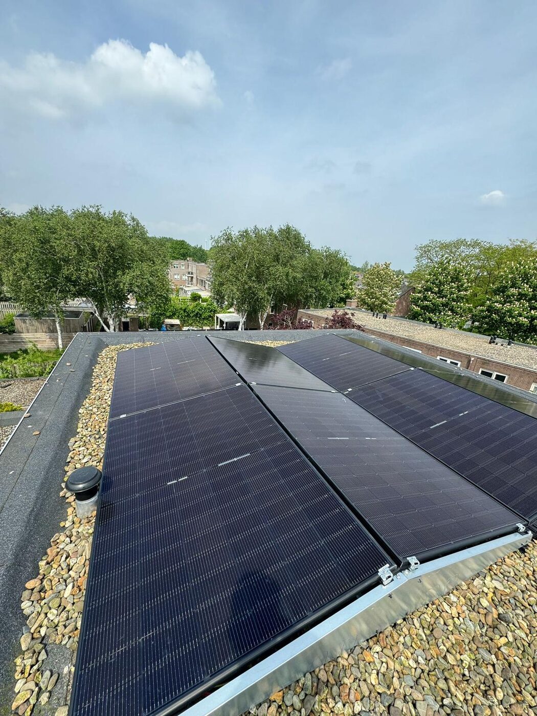 Zwarte zonnepanelen geinstalleerd op een plat dak met grindrand en groene omgeving op de achtergrond